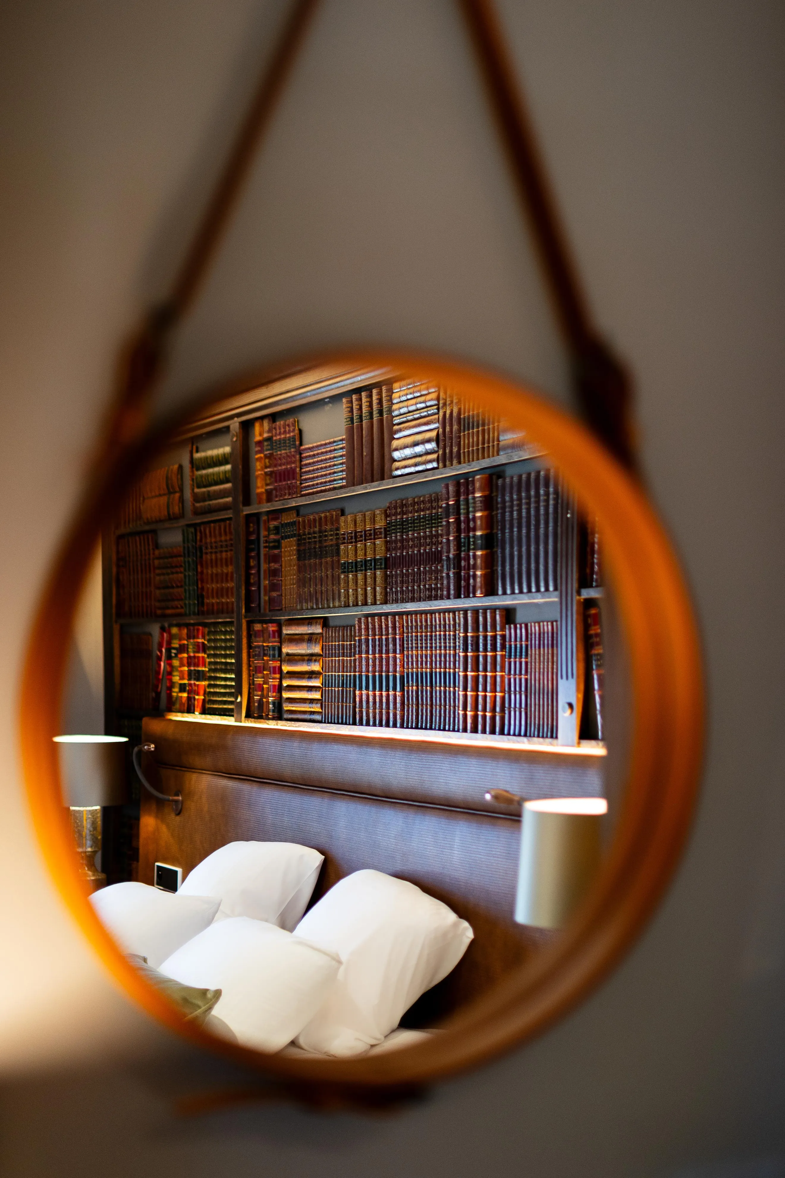 Viewed through a circular lens of a shelf filled with old books and a bed with white pillows