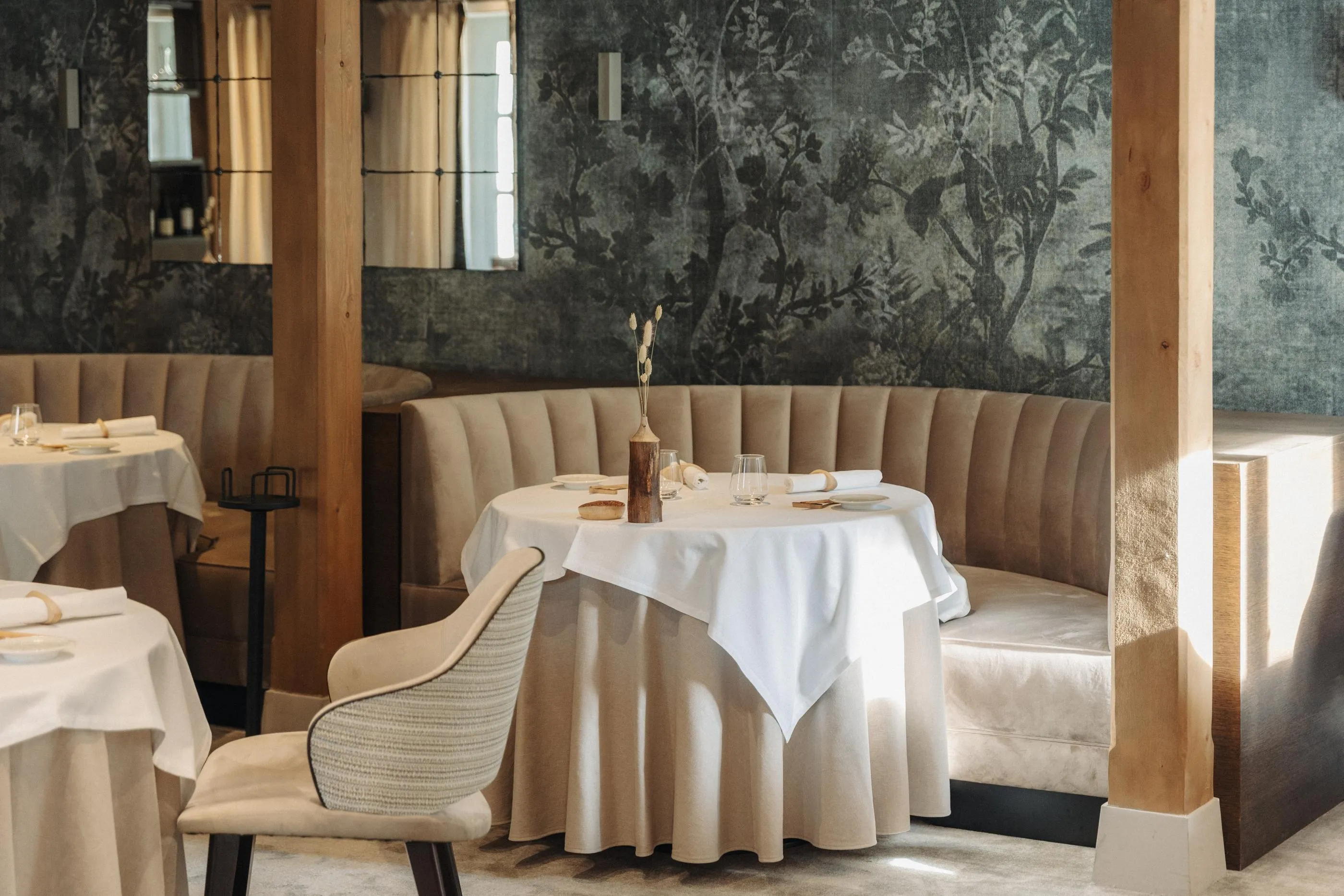 Une table dressée avec des verres et une décoration florale dans un restaurant aux murs ornés de motifs végétaux et aux banquettes rembourrées